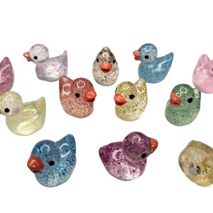 May include: A collection of 10 small, glittery rubber duck figurines in various colours, including pink, blue, green, yellow, and white.