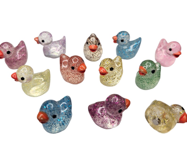 May include: A collection of 10 small, glittery rubber duck figurines in various colours, including pink, blue, green, yellow, and white.