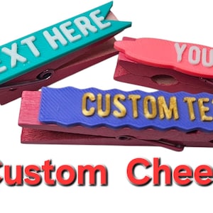 May include: Three wooden clothes pegs with colourful text overlays. One is teal with "YOUR TEXT HERE", another is pink with "YOUR TEXT", and the third is blue with "CUSTOM TEXT". The text "Custom Cheer Pin" is below.