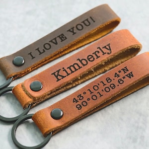 May include: Three leather keychains with black metal key rings. The first keychain is brown and says "I LOVE YOU!" The second keychain is brown and says "Kimberly". The third keychain is brown and says "43°10'18.4"N 90°01'09.6"W".