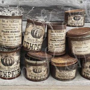 May include: A collection of vintage-style metal containers with aged labels. Some cans feature "Best Brand Pumpkin" and "Sweet Corn" labels. The containers are filled with decorative dried grass, creating a rustic, antique aesthetic.