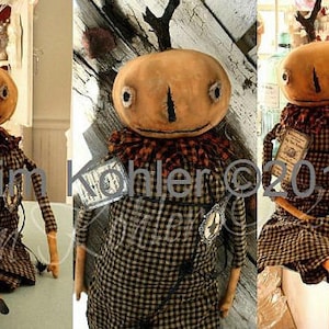 Peut inclure: Une poupée de chiffon faite à la main avec une tête de citrouille, portant une robe à carreaux et tenant un petit livre. La poupée a un corps long et fin et est assise sur une surface en bois. La tête de la poupée a un visage peint avec de grands yeux et une petite bouche. Les cheveux de la poupée sont faits de laine et sont coiffés en un simple chignon. La robe de la poupée est à carreaux en brun et noir. La poupée tient un petit livre avec une couverture brune et une étiquette blanche. Le livre porte le texte "Toad ©2012" sur l'étiquette. La poupée est assise sur une surface en bois avec un fond brun clair.