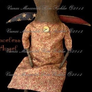 May include: A handmade rag doll with a brown head and limbs, wearing a red and white floral dress. The doll is sitting with its legs crossed and has a small, round, gold button on its chest. The doll is labeled "Faceless Angel" and "Veenas Mercantile Kim Kohler 2012".