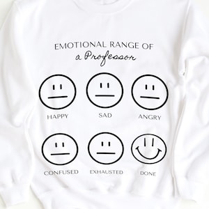 Puede incluir: Sudadera blanca con el texto "EMOTIONAL RANGE OF a Professor" y seis emoticonos negros que representan diferentes estados de ánimo: feliz, triste, enfadado, confundido, agotado y hecho.