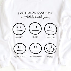 May include: White sweatshirt with the text "EMOTIONAL RANGE OF a Web Developer" above six black and white emoji faces representing different moods: happy, sad, angry, confused, exhausted, and done.