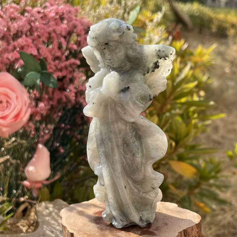 Pu&ograve; includere: Una statuetta di angelo intagliata in pietra di luna grigia e bianca. L'angelo &egrave; in piedi con le ali spiegate e le mani giunte in preghiera. La statuetta &egrave; alta circa 15 cm.