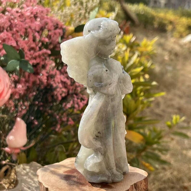 Pu&ograve; includere: Una statuetta di angelo scolpita in labradorite grigia. L'angelo ha le ali e sta in piedi con le mani giunte in preghiera. La statuetta &egrave; alta circa 15 cm.