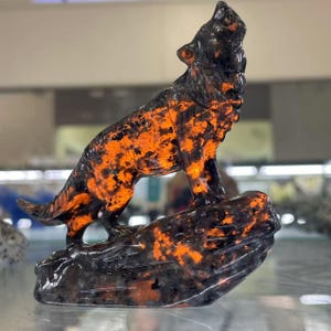 Puede incluir: Una escultura de lobo de obsidiana negra y naranja aullando a la luna, de pie sobre una base de roca.