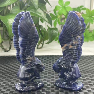 May include: Two blue and white carved angel figurines made of sodalite. The angels are kneeling with their wings spread out behind them.
