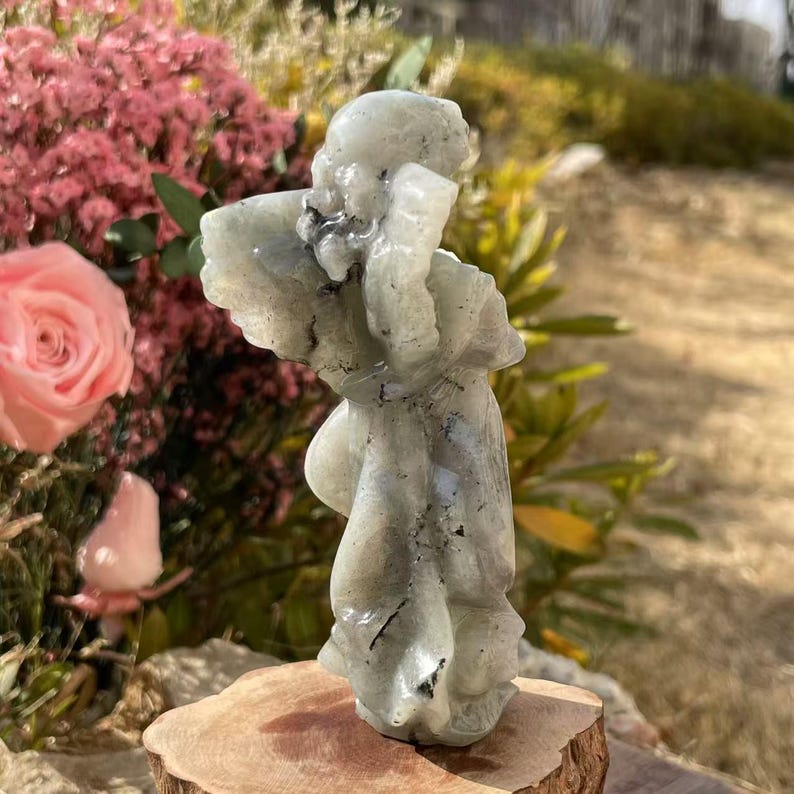 Pu&ograve; includere: Una statuetta di angelo intagliata in labradorite verde con inclusioni nere. L'angelo &egrave; in piedi su una base di legno.