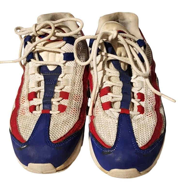 Puede incluir: Par de zapatillas deportivas con una parte superior de malla blanca, acentuada con detalles rojos y azules. Los zapatos tienen cordones blancos y una puntera azul. El dise&ntilde;o incluye detalles rojos en los laterales y una franja azul en el centro.