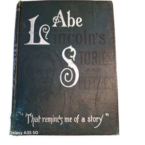 May include: A vintage book titled "Abe Lincoln's Stories and Speeches" with a dark teal cover. The title is in white, stylized lettering. A portrait of Abraham Lincoln is faintly visible. The quote "That reminds me of a story" is at the bottom.