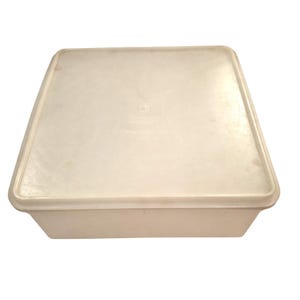 May include: A square, off-white plastic storage container with a matching lid. The container features a flat, smooth top surface with a slightly raised rim around the edges and a deep, solid base, providing a simple and functional design for storage.