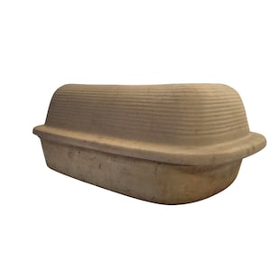 May include: A beige, rectangular container with a rounded, ribbed lid. The container has a slightly curved shape and appears to be made of a natural, possibly biodegradable material. The overall design is simple and functional.