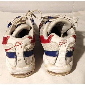 Puede incluir: Par de zapatillas Nike Air Max 95 blancas, rojas y azules. Las zapatillas tienen una parte superior de malla con detalles en rojo y azul, una entresuela blanca y una unidad Air visible. El logotipo de Nike es visible en el tal&oacute;n.