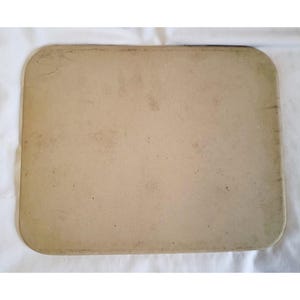 May include: A rectangular, light brown baking stone with rounded corners. The stone has a slightly textured surface and shows signs of use. The edges are darker, and the overall appearance suggests it's been well-used for baking.