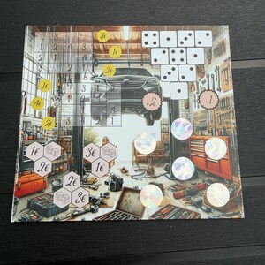 May include: A rectangular board game sheet featuring a garage scene with a car on a lift, tools, and workbenches. The design includes various game elements such as dice icons, numerical values with euro symbols, hexagonal grids, and holographic circular stickers.