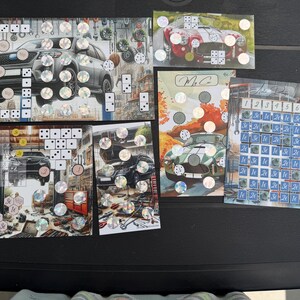May include: A collection of five rectangular game boards featuring automotive themes, including illustrations of cars in garages, dice patterns, holographic circular stickers, and a grid labeled with numbers one through six and currency symbols.