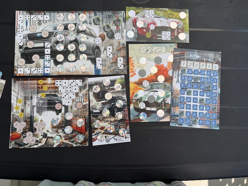 May include: A collection of five rectangular game boards featuring automotive themes, including illustrations of cars in garages, dice patterns, holographic circular stickers, and a grid labeled with numbers one through six and currency symbols.