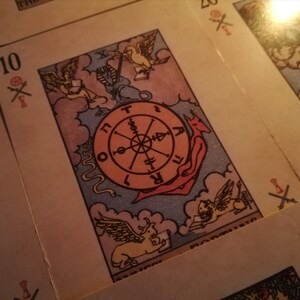 Close-up of a vintage tarot card from a tarot reading deck, featuring the Wheel of Fortune surrounded by symbolic figures and astrological elements. The warm, dim lighting creates a mystical atmosphere associated with psychic medium practices. The image represents destiny, cycles of change, spiritual insight, and future reading guidance through traditional tarot symbolism.