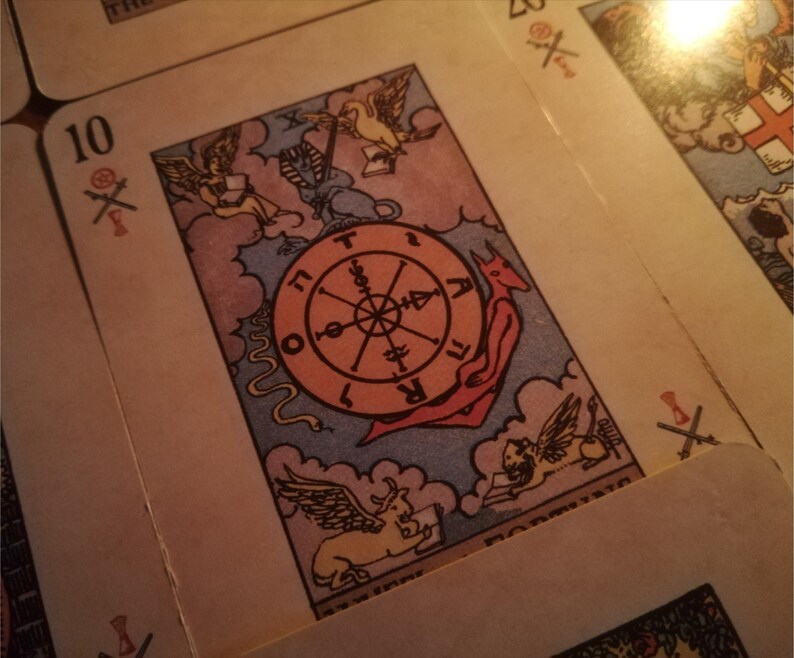 Close-up of a vintage tarot card from a tarot reading deck, featuring the Wheel of Fortune surrounded by symbolic figures and astrological elements. The warm, dim lighting creates a mystical atmosphere associated with psychic medium practices. The image represents destiny, cycles of change, spiritual insight, and future reading guidance through traditional tarot symbolism.
