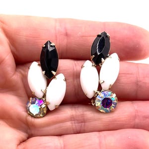 May include: A pair of earrings featuring a cluster of marquise-cut black and white stones, accented by a single round iridescent crystal at the base. The stones are set in a gold-tone metal frame, creating a multi-faceted design with contrasting colors.
