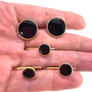 May include: A set of five gold-toned metal accessories featuring circular black inlays. The collection includes two larger circular pieces and three smaller circular pieces attached to horizontal metal bars, all displaying a smooth, polished finish.