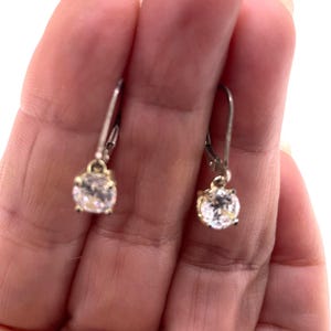 May include: A pair of silver-toned leverback earrings, each featuring a single round, clear, faceted stone set in a four-prong metal basket. The earrings have a polished metallic finish and a classic drop design that hangs from a secure hinged closure.