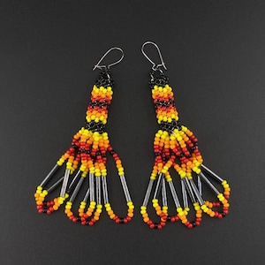 May include: A pair of long beaded earrings with black, red, yellow, and silver beads. The earrings are dangling and have a fringe-like design.