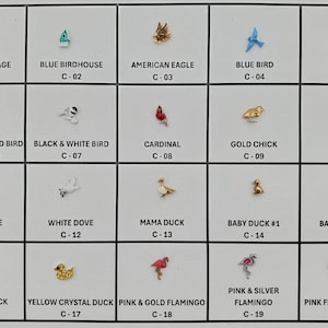 May include: A grid of small, decorative bird and animal charms. The charms include a gold bird cage, blue birdhouse, American eagle, blue jay, and various birds and ducks. Each charm is labeled with a letter and number.