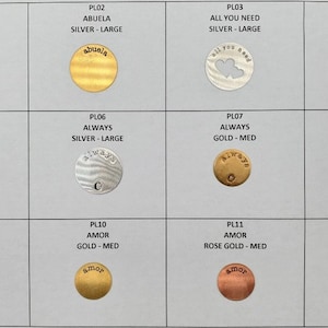Peut inclure: Douze disques métalliques ronds avec différents mots et motifs. Les disques sont de différentes couleurs, notamment or, argent et or rose. Les mots sur les disques incluent "Abuela", "Always" et "Amor".