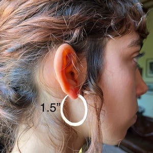 May include: A circular hoop earring with a smooth, polished metallic finish. The earring has a diameter of 3.81 cm as indicated by the text overlay. The hoop is a simple, continuous ring design that hangs from the earlobe, featuring a reflective surface.