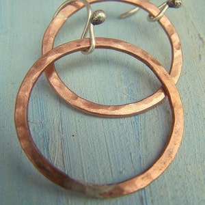 Puede incluir: Un par de pendientes de aro de cobre martillado con cierres de plata. Los pendientes son un diseño simple pero elegante.