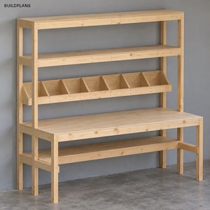 May include: A light-colored wooden workbench featuring a large flat work surface, a lower storage shelf, and an upper hutch with a long top shelf and a middle section divided into seven open compartments. The text BUILDPLANS is visible.