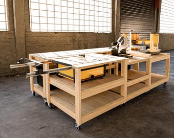 Può includere: Un grande banco da lavoro in legno con una sega da tavolo integrata e altri utensili elettrici. Il banco da lavoro è di colore chiaro, con una sega da tavolo gialla e altri utensili gialli. Il banco da lavoro ha ripiani ed è su ruote.