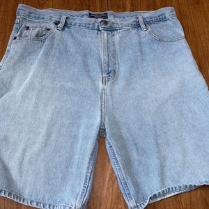 May include: Light blue denim shorts with a classic five-pocket design. The shorts have a button and zipper closure, belt loops, and a faded wash. The shorts are made of a sturdy denim material.