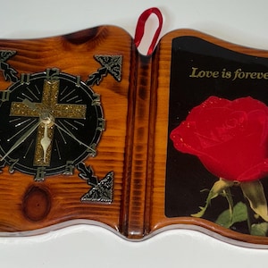 May include: Wooden book-shaped wall clock with a clock face and a red rose image. The clock face has a cross design. The right side has a red rose with the text "Love is forever".
