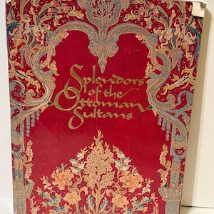 May include: A hardcover book titled "Splendors of the Ottoman Sultans." The cover is a vibrant red with ornate gold and floral designs. The title is in gold script, and the overall aesthetic is historical and decorative.