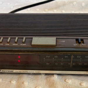 Puede incluir: Un radio reloj digital PM/AM Emerson vintage con un acabado de madera marr&oacute;n oscuro. Incluye una pantalla digital, un dial de frecuencia de radio y botones para hora, minuto, despertar y dormir. El reloj tiene una bater&iacute;a de respaldo.