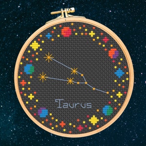 May include: A round embroidery hoop with a black fabric background featuring a colourful constellation design of Taurus, the bull. The constellation is outlined in blue thread and surrounded by colourful stars and dots.