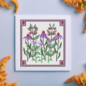 Peut inclure: Un motif de point de croix représentant un motif floral violet et vert avec des accents rouges. Le motif est encadré d'une bordure violette.
