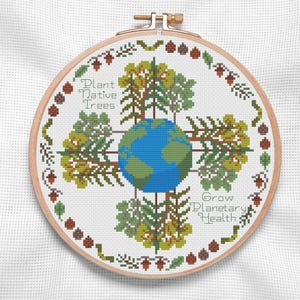 May include: A cross-stitch embroidery hoop featuring a globe surrounded by trees and the text "Plant Native Trees" and "Grow Planetary Health." The design includes green, blue, and brown elements, with a decorative border of leaves and acorns.