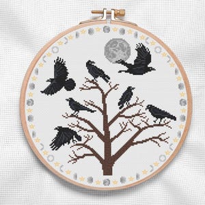May include: A cross-stitch pattern featuring a stylized tree with eight black crows perched on its branches. The tree is surrounded by a circle of yellow stars and gray moons.
