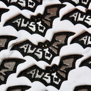 May include: Multiple black felt bat-shaped patches with silver embroidery that reads "AUSTO" in a stylized font.