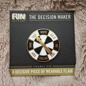 May include: A gold enamel pin featuring a black and white decision wheel with the words "Yup", "Nah", "Yep", "No Way", "Yes", "Do It", "No", and "Nope". The pin is on a black and white card with the text "FUN SUPREME™ THE DECISION MAKER" and "A DECISIVE PIECE OF WEARABLE FLAIR".