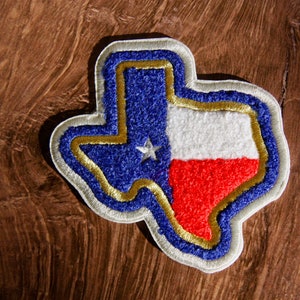 Könnte beinhalten: Ein Filz-Patch in Form des Bundesstaates Texas mit den Farben der Texas-Flagge: Blau, Weiß und Rot. Der Patch hat einen goldenen Umriss und einen weißen Rand.