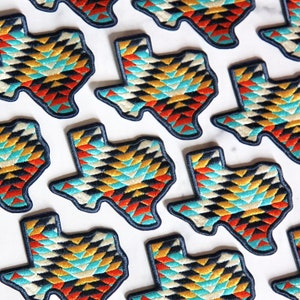 May include: Multiple colorful embroidered patches shaped like the state of Texas. The patches feature a geometric pattern in shades of blue, red, yellow, and white.