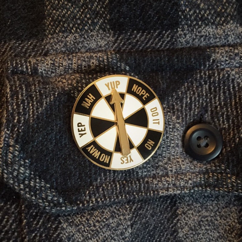 May include: A gold-colored pin with a black and white wheel that has the words "Yup", "Nope", "Do It", "No", "Yes", "No Way", "Yep", and "Nah" printed around the edge. The wheel has a gold arrow pointing to the word "Yes".