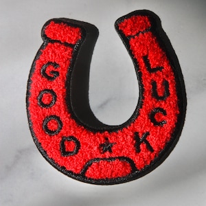 May include: Red felt horseshoe patch with black stitching and the words "GOOD LUCK" written on it.