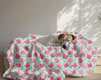 Könnte beinhalten: Eine hellblaue und rosafarbene gemusterte Fleece-Decke mit einem schlafenden Hund darauf. Die Decke hat ein sich wiederholendes Muster aus rosafarbenen Katzenköpfen mit goldenen Akzenten.